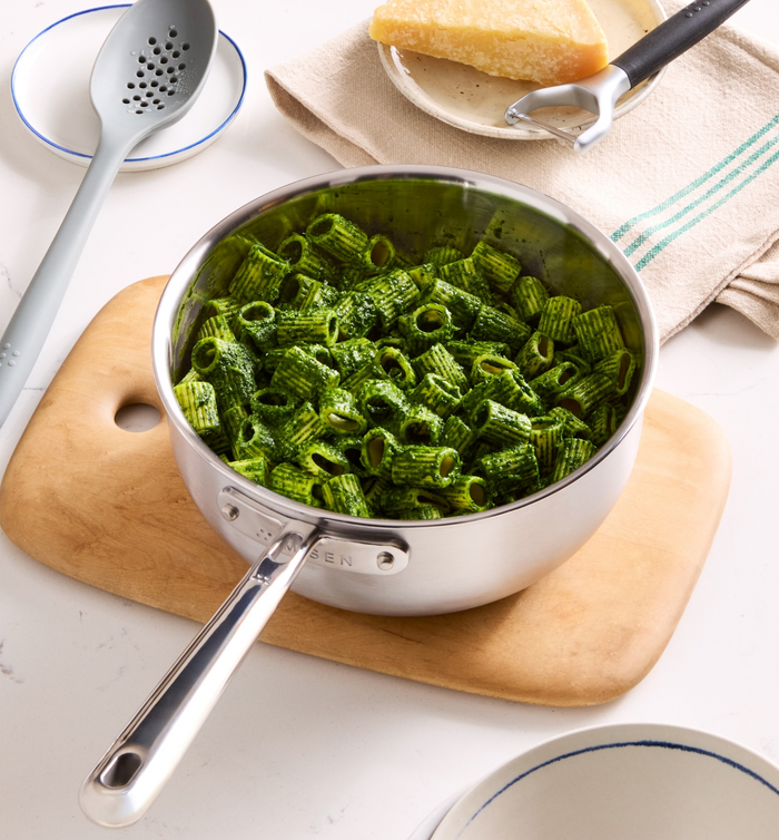 Rigatoni pasta with green pesto sauce in stainless steel saucepan on wooden cutting board