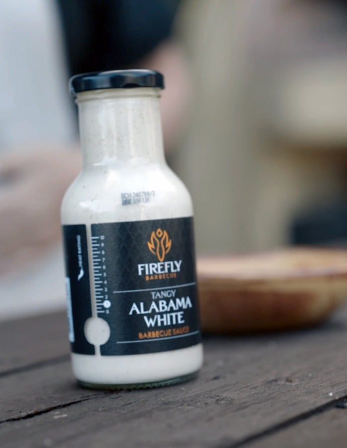 Close-up of Firefly Alabama White BBQ Sauce bottle on a wooden table, emphasizing its tangy, creamy profile for grilling and dipping.