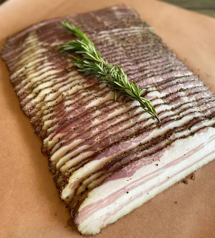 Sliced bacon with rosemary and black pepper on cutting board