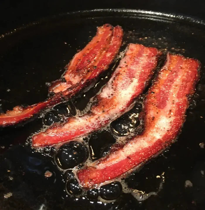 Crispy bacon strips frying in a pan