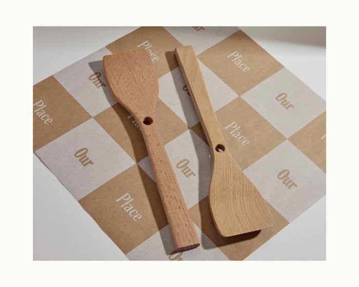 Two Beechwood Spatulas with handle holes rest on brown-and-white checkered Our Place paper, ideal as Always Pan nesting spatula accessories.