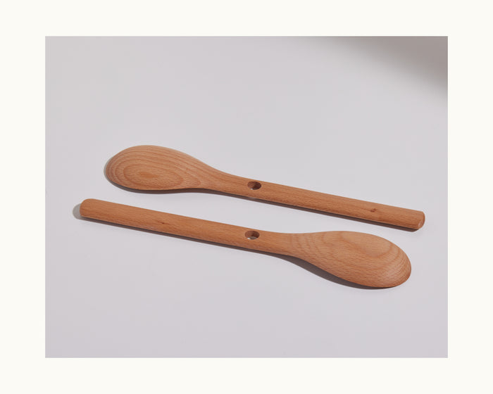 Two Beechwood Spoons with handle holes are placed side by side on a plain white surface, combining usefulness with an attractive natural wood design for your kitchen.