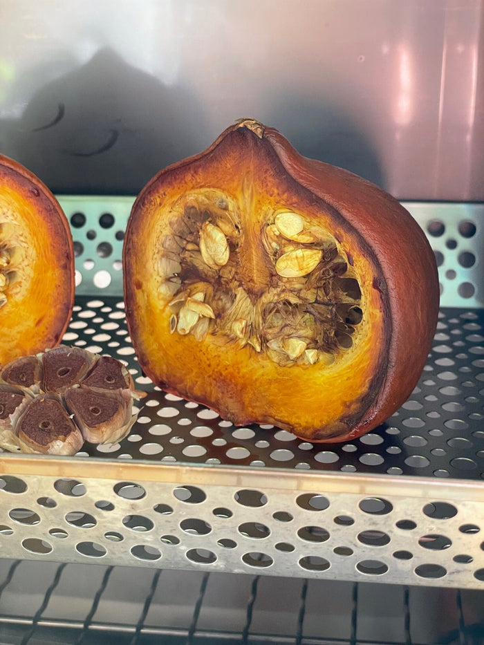 Halved pumpkin on stainless steel smoker tray in outdoor grill