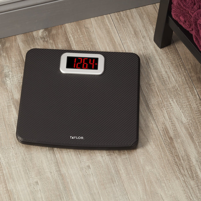 Carbon fiber digital bathroom scale on a wooden floor, displaying 126.4 lb