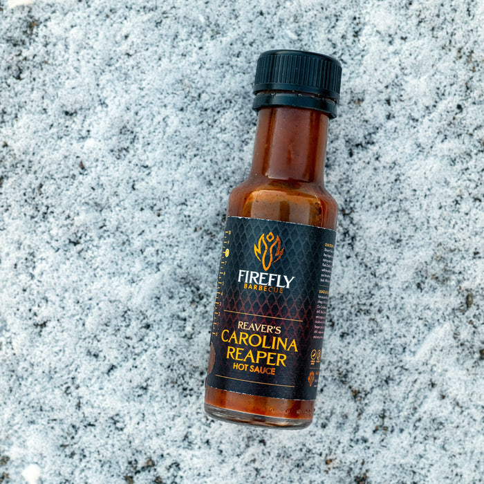 Firefly BBQ Carolina Reaper Hot Sauce bottle lying on a snowy surface, showcasing the intense heat contrast. Perfect for extreme spice lovers.