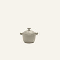 The Petite Perfect Pot, in beige with dual side handles and a lid, is centered against a plain off-white background.