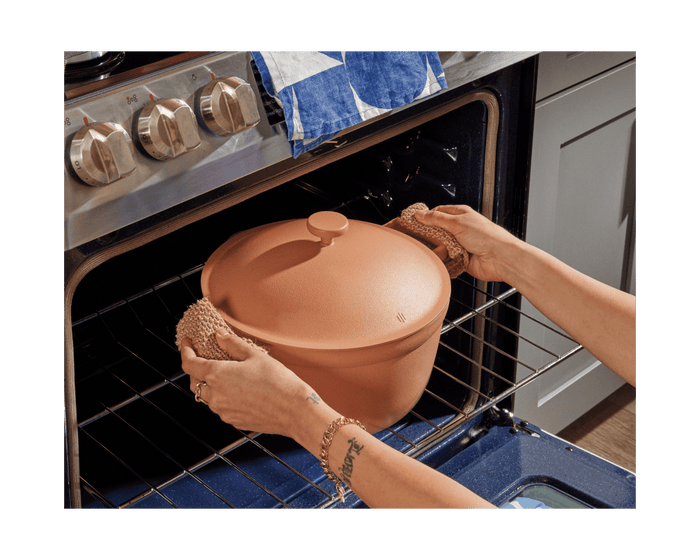 A person uses mitts to place the covered Cookware Duo terracotta pot, part of a bestselling set, into the oven by holding its handles.