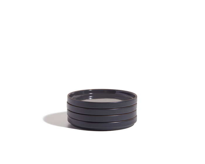 A stack of four round, dark-colored Dessert Plates, resembling sleek demi plate tableware, rests on a white background.