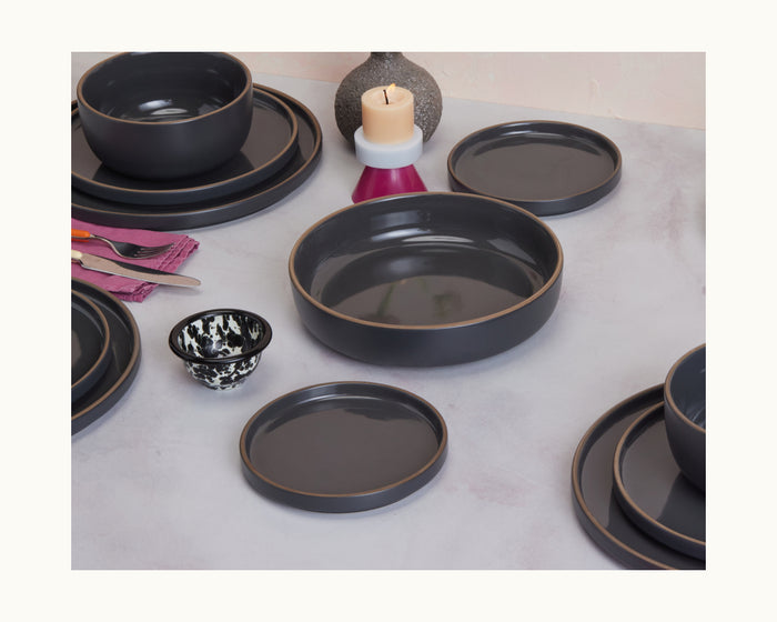 A stylish set of Dessert Plates in dark gray ceramic, beautifully arranged on a light-colored table with a candle, small vase, utensils, and a patterned cup.
