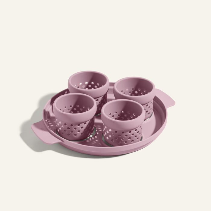 The Egg Poacher features four mauve silicone cups for poaching eggs, set on a round handled tray, all made from durable plastic.
