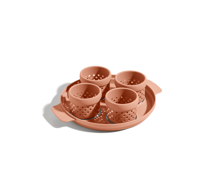 The Egg Poacher features four terracotta-colored, perforated silicone cups on a matching handled tray—ideal for poaching eggs—shown against a white background.