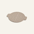 The Fearless Fry is a beige round silicone steamer insert with two side handles and multiple small holes, designed to fit perfectly in the Always Pan or to be used as a versatile frying tool.