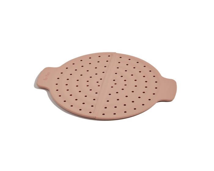 The Fearless Fry is a round, pink silicone steamer basket with perforated holes and two handles, shown on a white background—ideal for pairing with your Always Pan or using as a versatile frying tool.