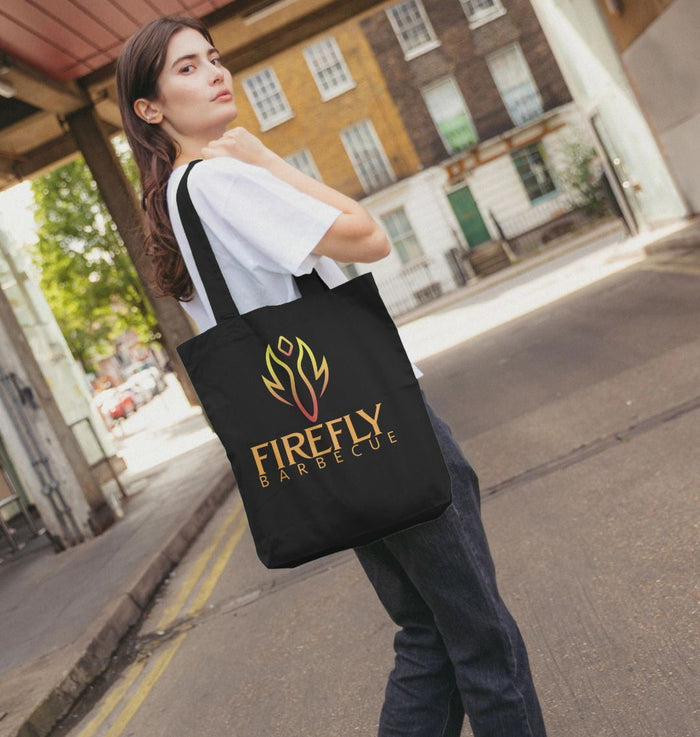 Woman carrying black tote bag with Firefly Barbecue logo outdoors