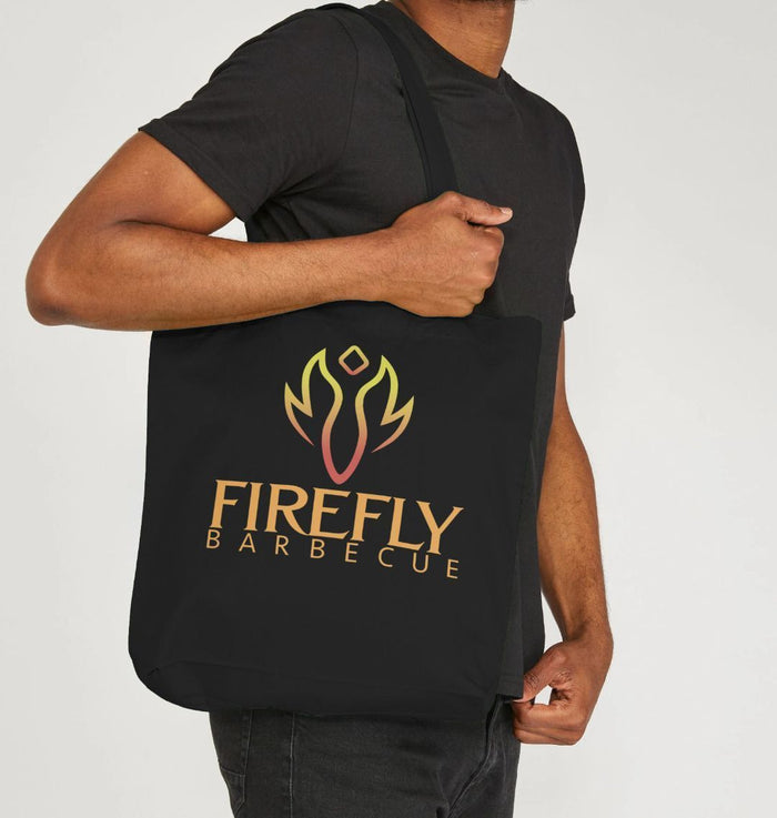 Man holding black tote bag with Firefly Barbecue logo indoors