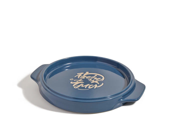 The Flipping Platter is a round blue ceramic dish with side handles and white stylized Korean writing inside—ideal for serving dishes such as maqluba or tahdig.