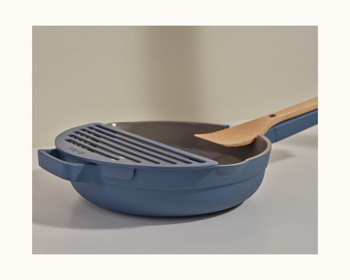 The Fry Deck by Our Place is a blue nonstick skillet paired with a grill insert and wooden spatula, all on a light surface—an ideal frying upgrade for your kitchen.