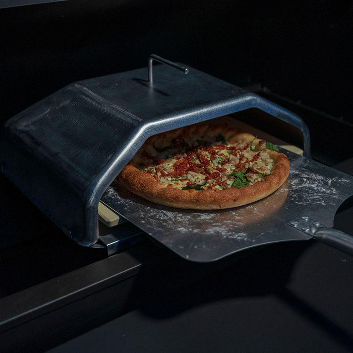 Pizza being cooked in outdoor grill with pizza attachment