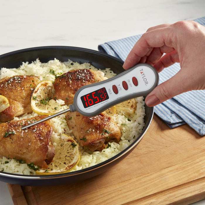 Thermometer inserted into a pan of roasted chicken and rice with lemon slices and fresh herbs nearby