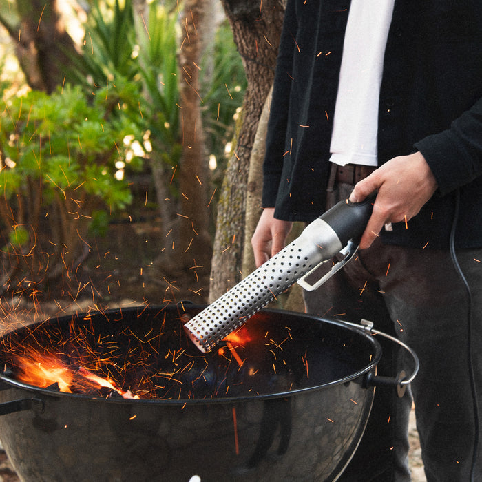 Person igniting firewood with electric firelighter outdoors
