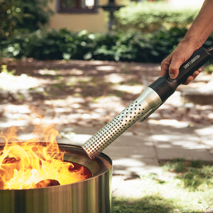 Hand holding electric firelighter igniting a barbecue grill