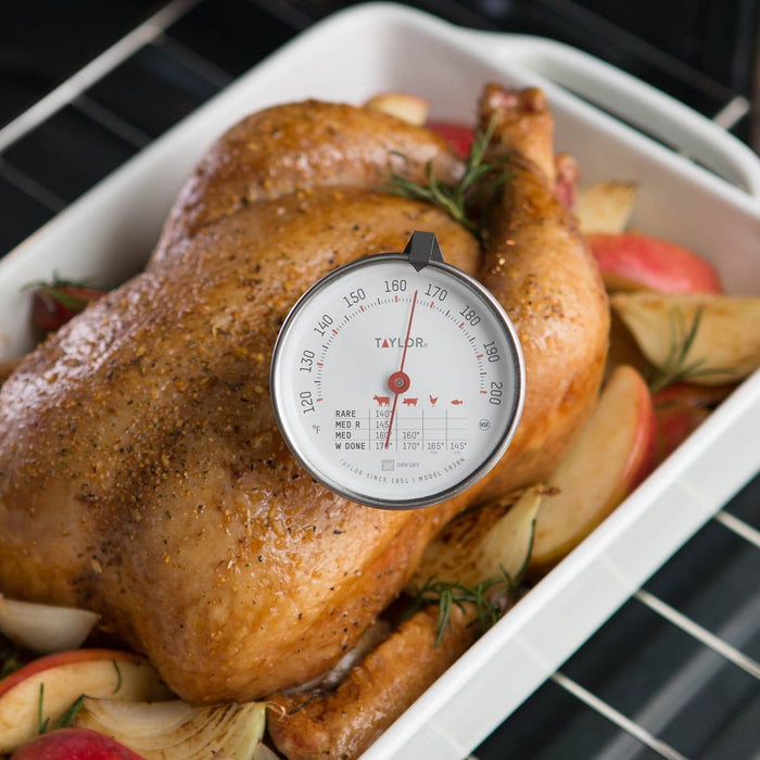 Taylor meat thermometer over a roasted turkey in a white roasting pan with rosemary and apples
