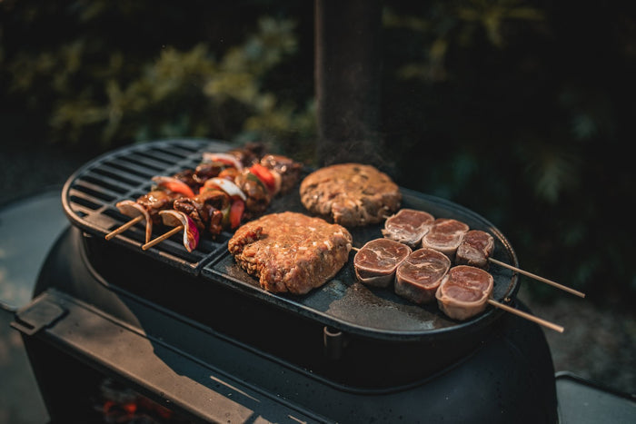 Outdoor grill with skewers, burger patties, and lamb chops cooking at night