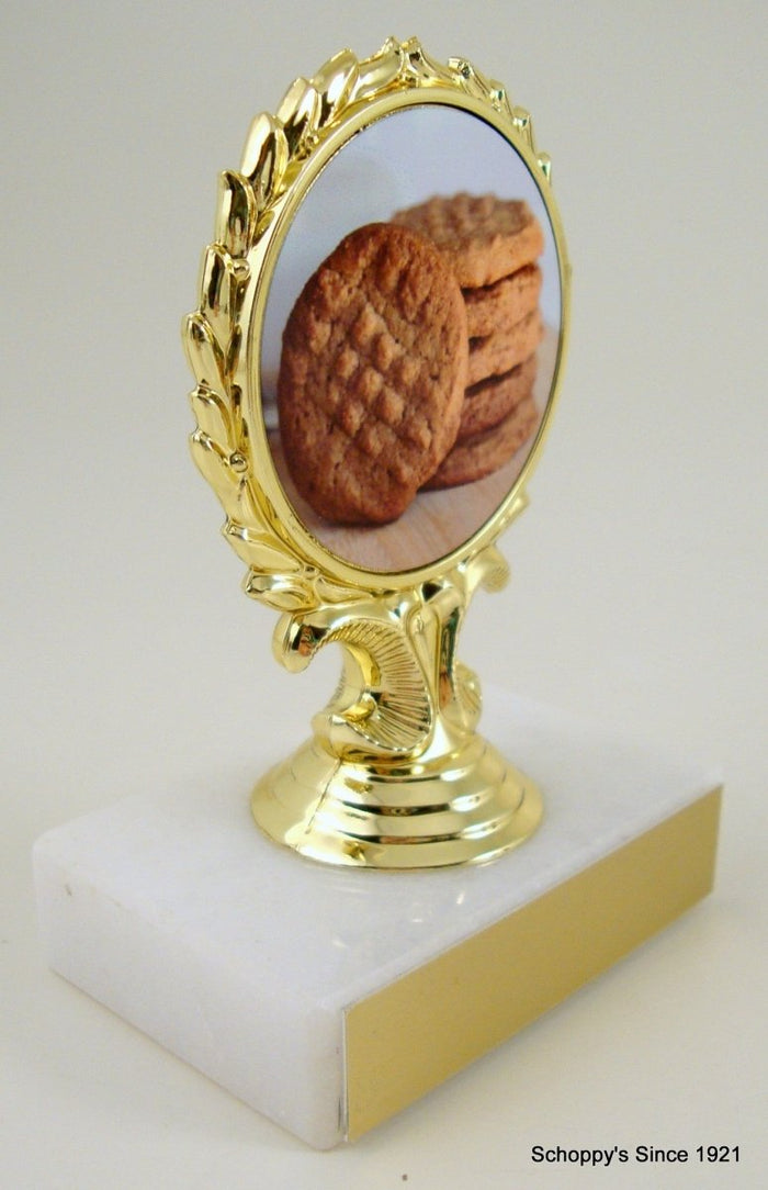 A trophy featuring a three-dimensional peanut character in the center, with a gold-colored award ribbon above it, mounted on a white base.