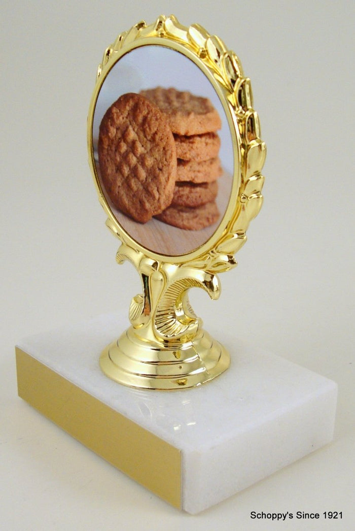 A trophy featuring a three-dimensional peanut character in the center, with a gold-colored award ribbon above it, mounted on a white base.