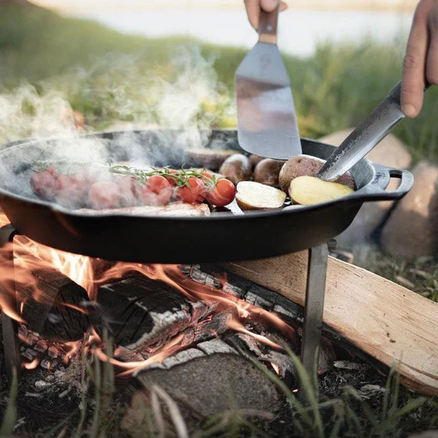 Outdoor cooking with cast iron skillet over campfire