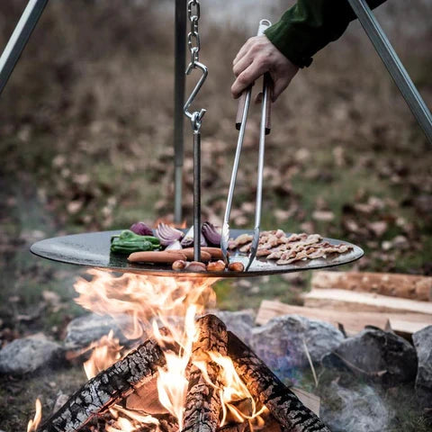 Person using Petromax BBQ coal tongs to handle food over a campfire