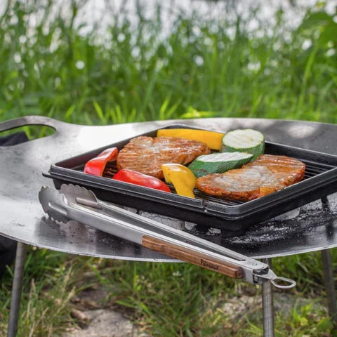 Petromax BBQ coal tongs placed on a grill with food for outdoor barbecue
