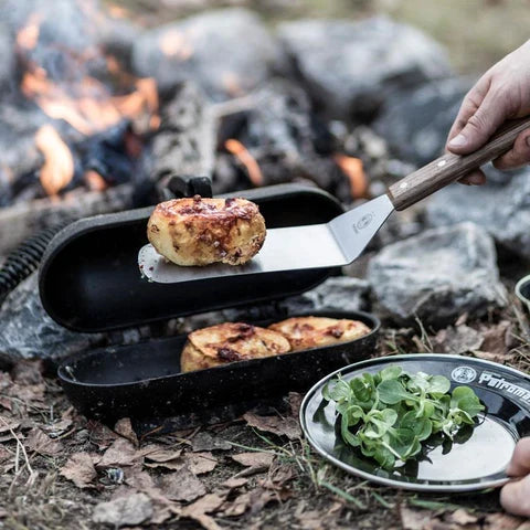 Person using Petromax spatula to flip food on outdoor campfire grill