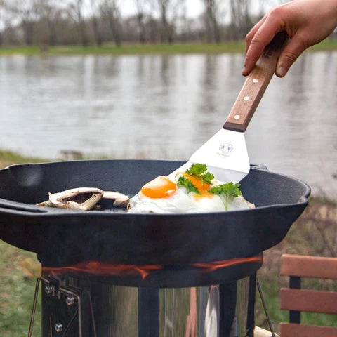 Petromax stainless spatula flipping eggs on outdoor grill with long handle