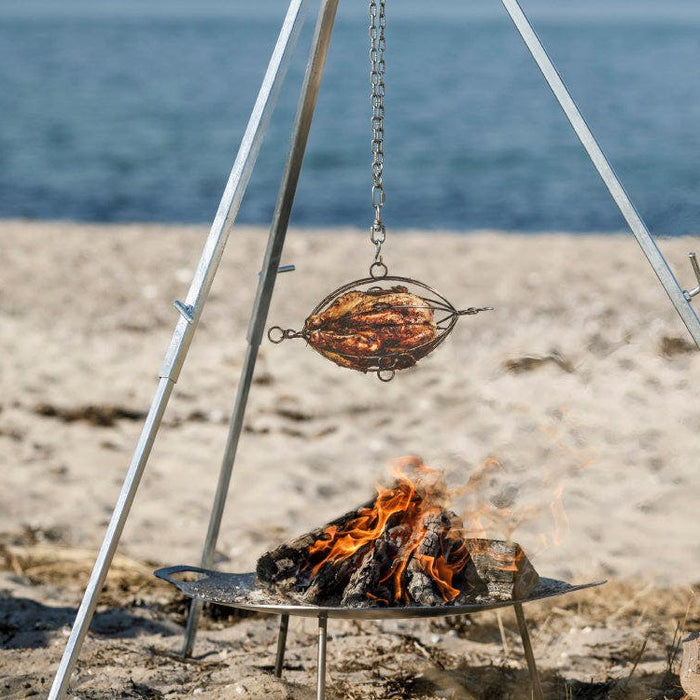 Wood being smoked over a campfire on a beach with ocean in the background