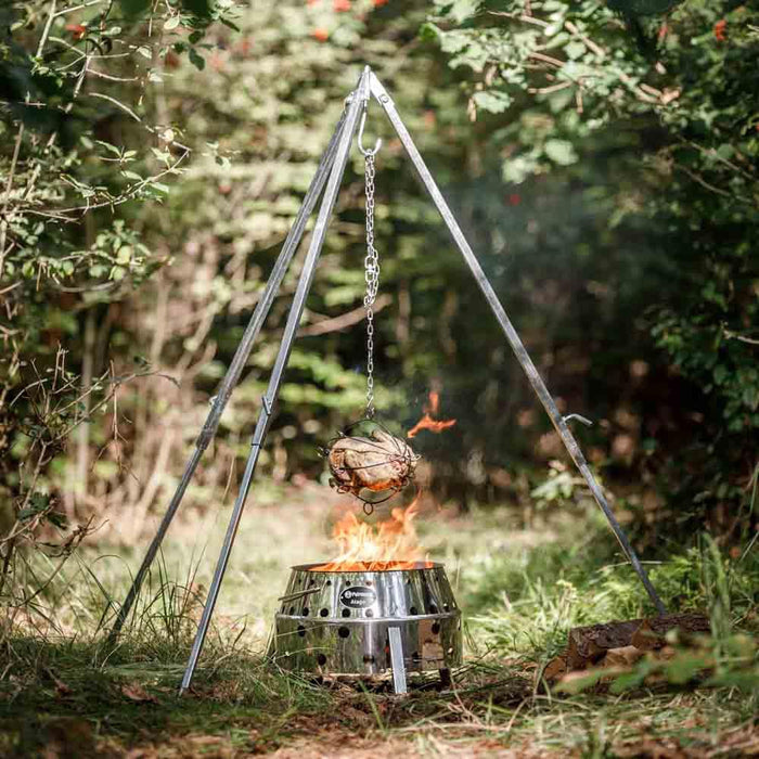 Metal tripod fire pit with hanging pot over flames in a forest setting