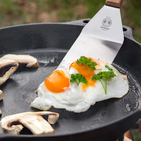 Fried egg with short handle spatula and mushrooms on outdoor grill