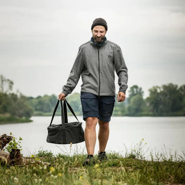 Man carrying a black Petromax transport bag with outdoor gear near a river