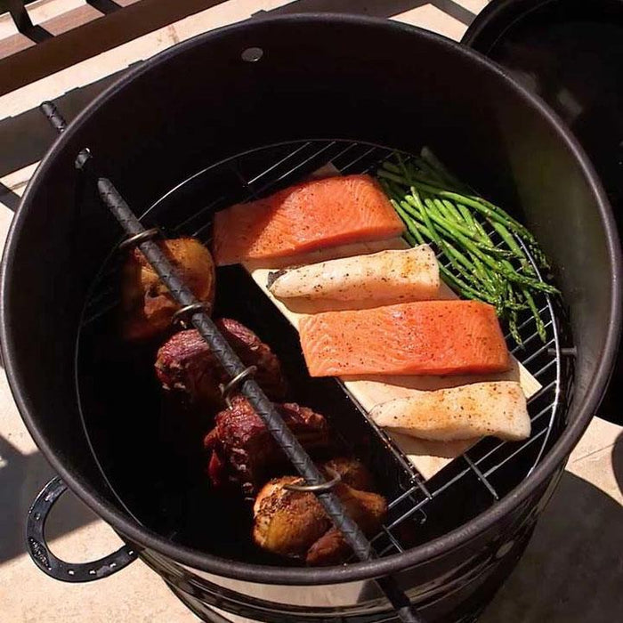 Pit Barrel Hinged Grate in use with salmon, cod, and asparagus grilling while meats hang, showcasing versatile cooking in outdoor smoker setup.