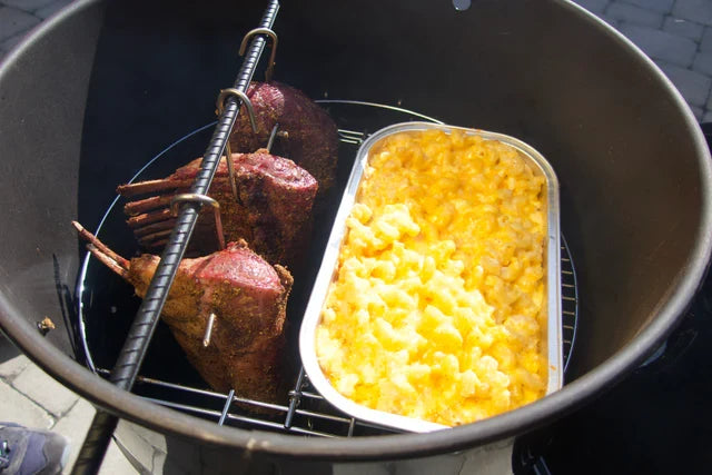 Pit Barrel Hinged Grate in action with smoked lamb and mac and cheese tray, showing multi-zone cooking in outdoor drum smoker.