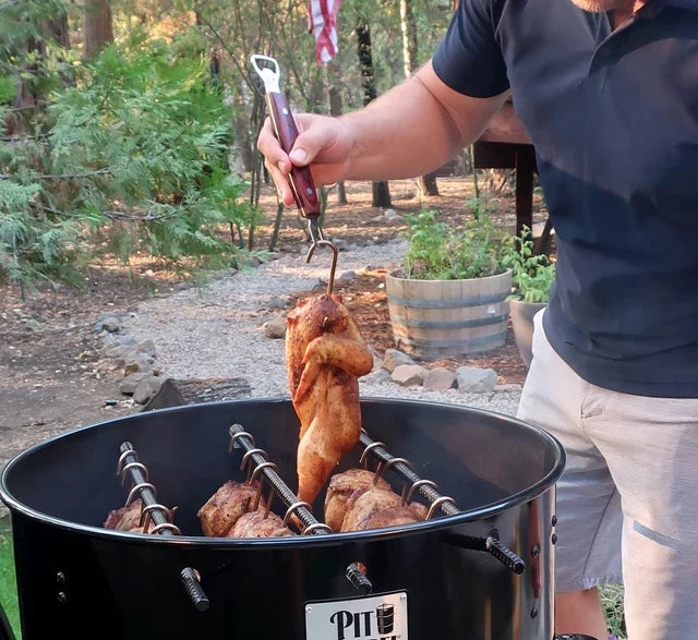 Man using Pit Barrel Ultimate Hook Tool - FireFly Barbecue to lift whole chicken from outdoor smoker, showcasing its grilling utility.