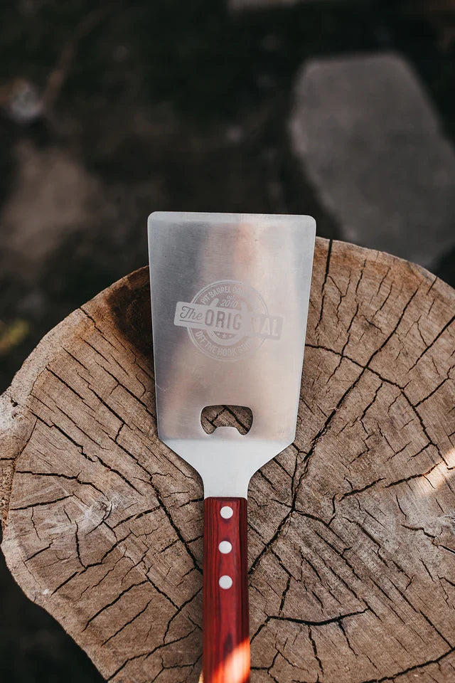 Pit Barrel Spatula with wood handle on chopped wood log for outdoor cooking