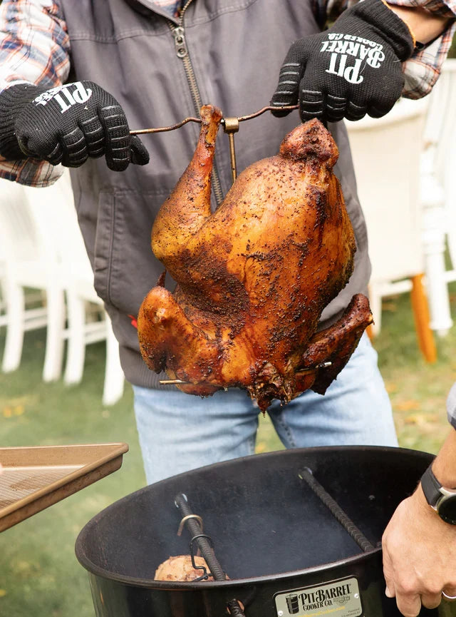 Cooked turkey being lifted from a Pit Barrel Cooker using the Pit Barrel Stainless Steel Poultry Hanger - FireFly Barbecue outdoor grill tool.