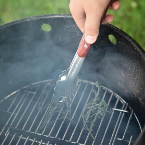 Hand using tongs to flip food on grill
