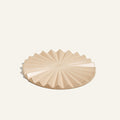 The Pleat Trivet, a beige, round ceramic piece with a radial, pleated pattern, is displayed on a plain light background.