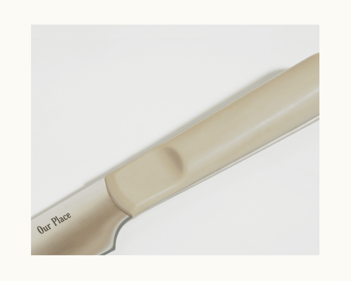 Close-up of the Precise Paring Knife, featuring a beige handle and ultra sharp German steel blade engraved with "Our Place," displayed on a white background.
