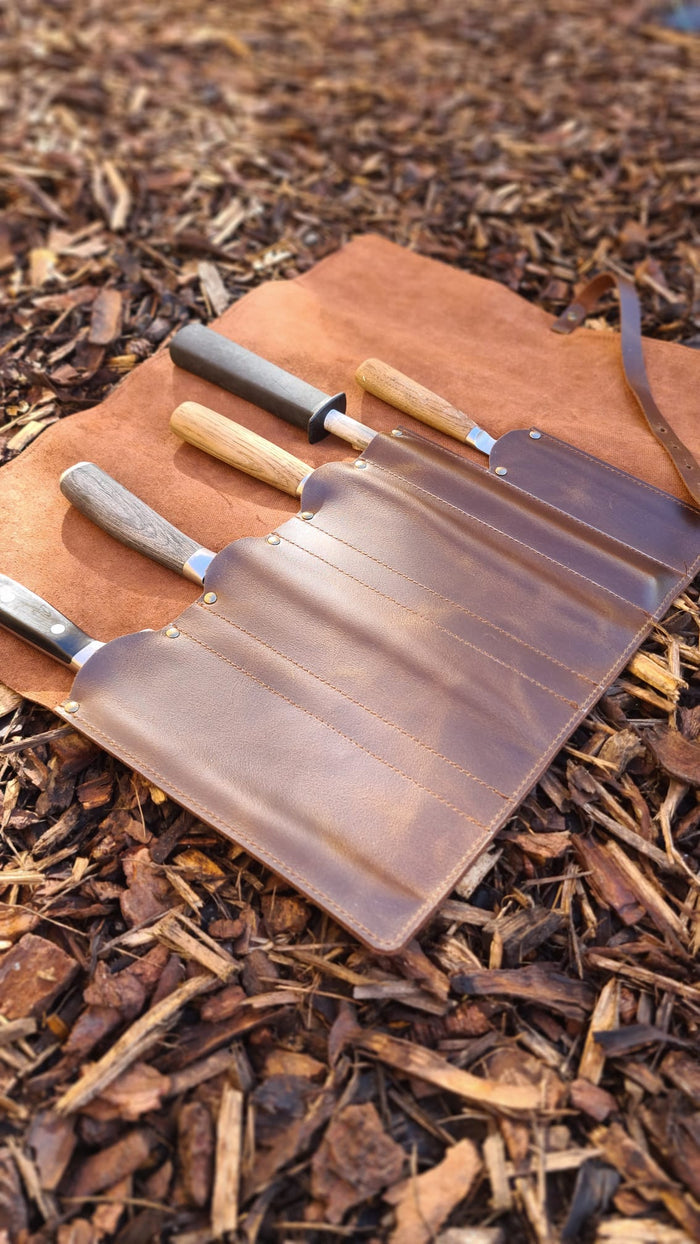 Set of outdoor knives in leather roll on wood chips