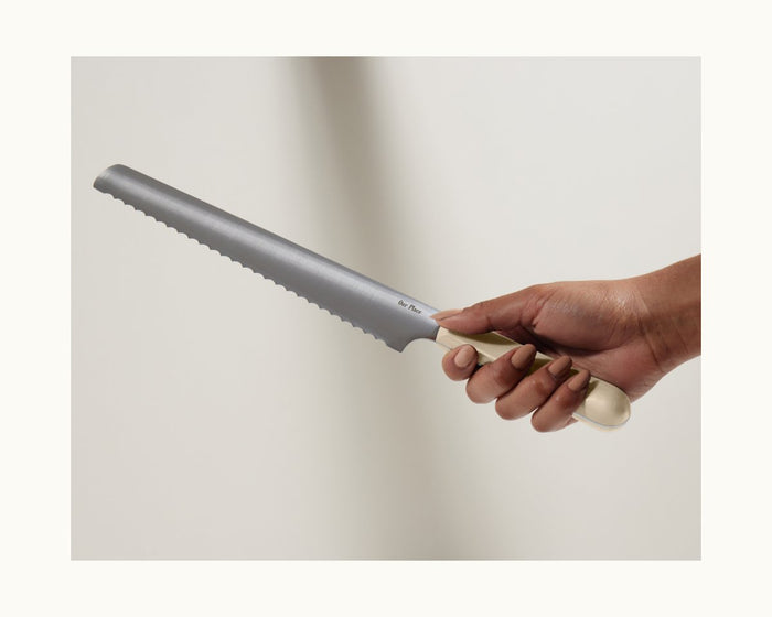 A hand holds the Serrated Slicing Knife, featuring a cream handle and an ultra-sharp German steel blade, against a neutral background.