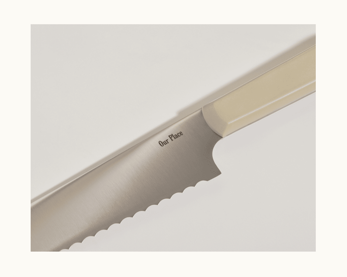 A close-up of the Serrated Slicing Knife, featuring an ultra-sharp premium German steel blade engraved with the Our Place brand name and a beige handle.