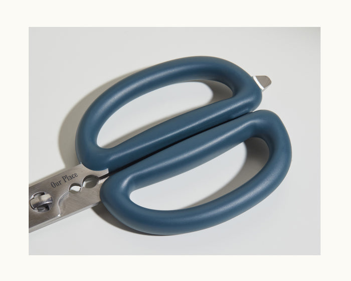 Close-up of Shear Genius kitchen shears with blue handles and metal blades, showcasing their multifunctional design, photographed on a white background.